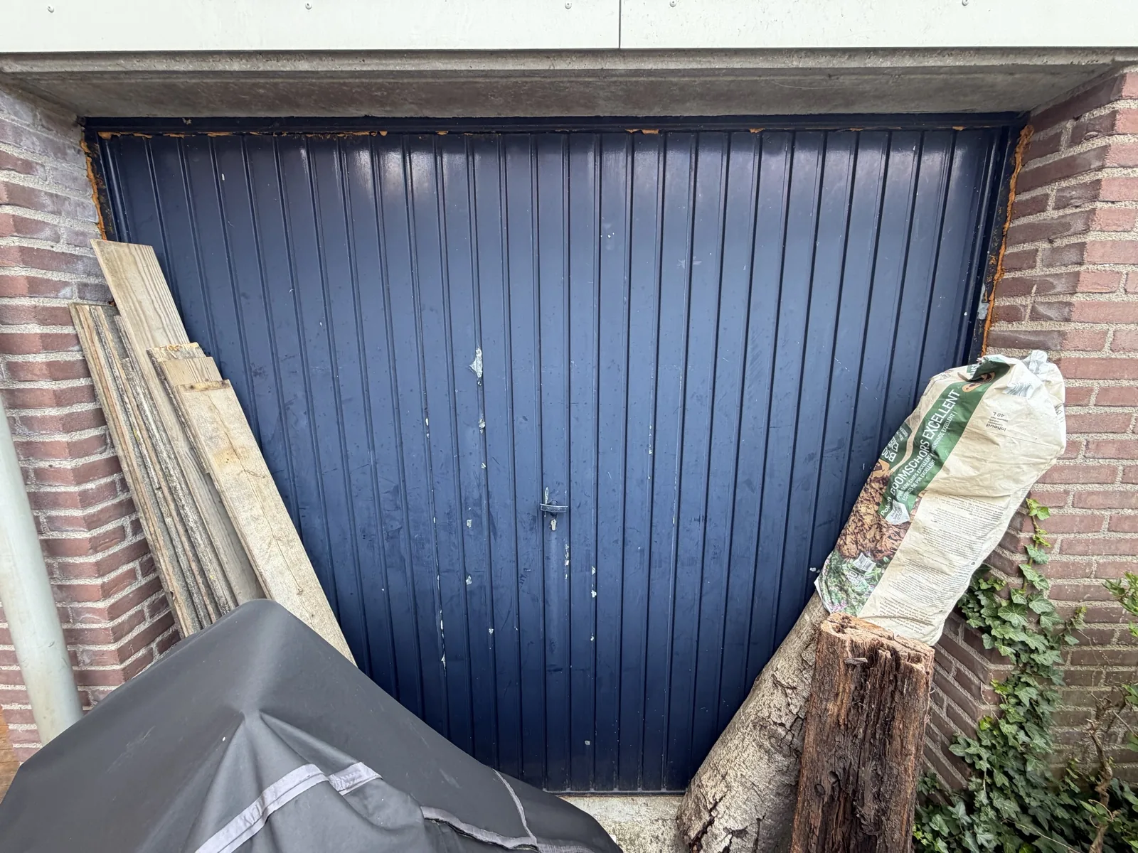 Oude blauw geschilderde stalen kanteldeur in de bestaande gemetselde garageopening