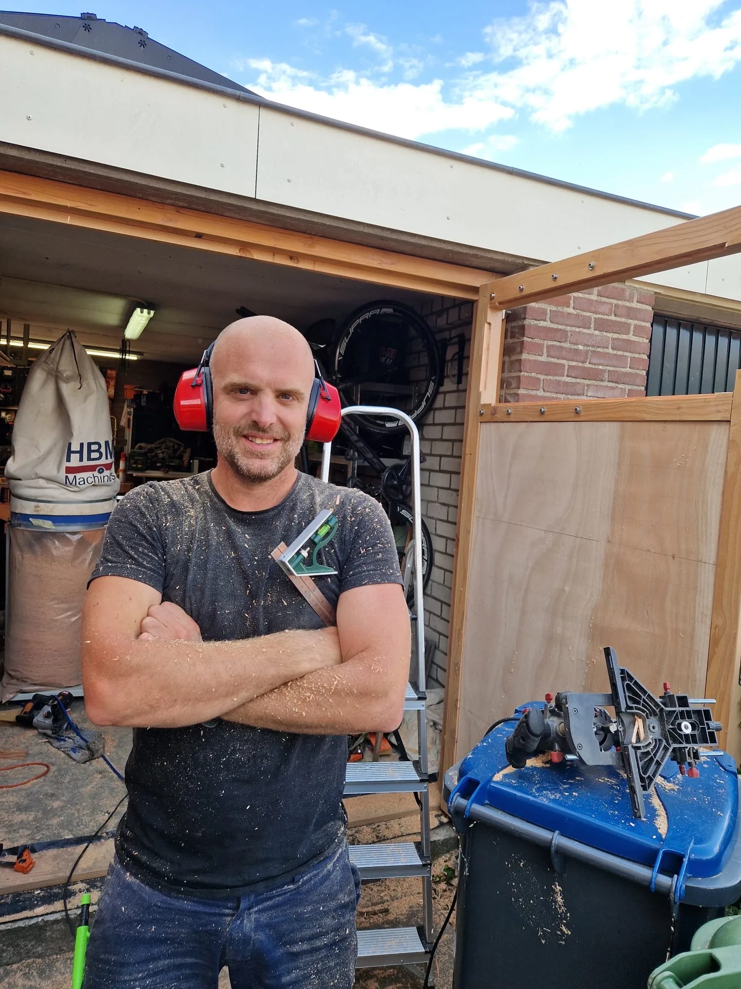 Bas Bartholomeus voor de geopende garagedeuren, met gehoorbescherming om