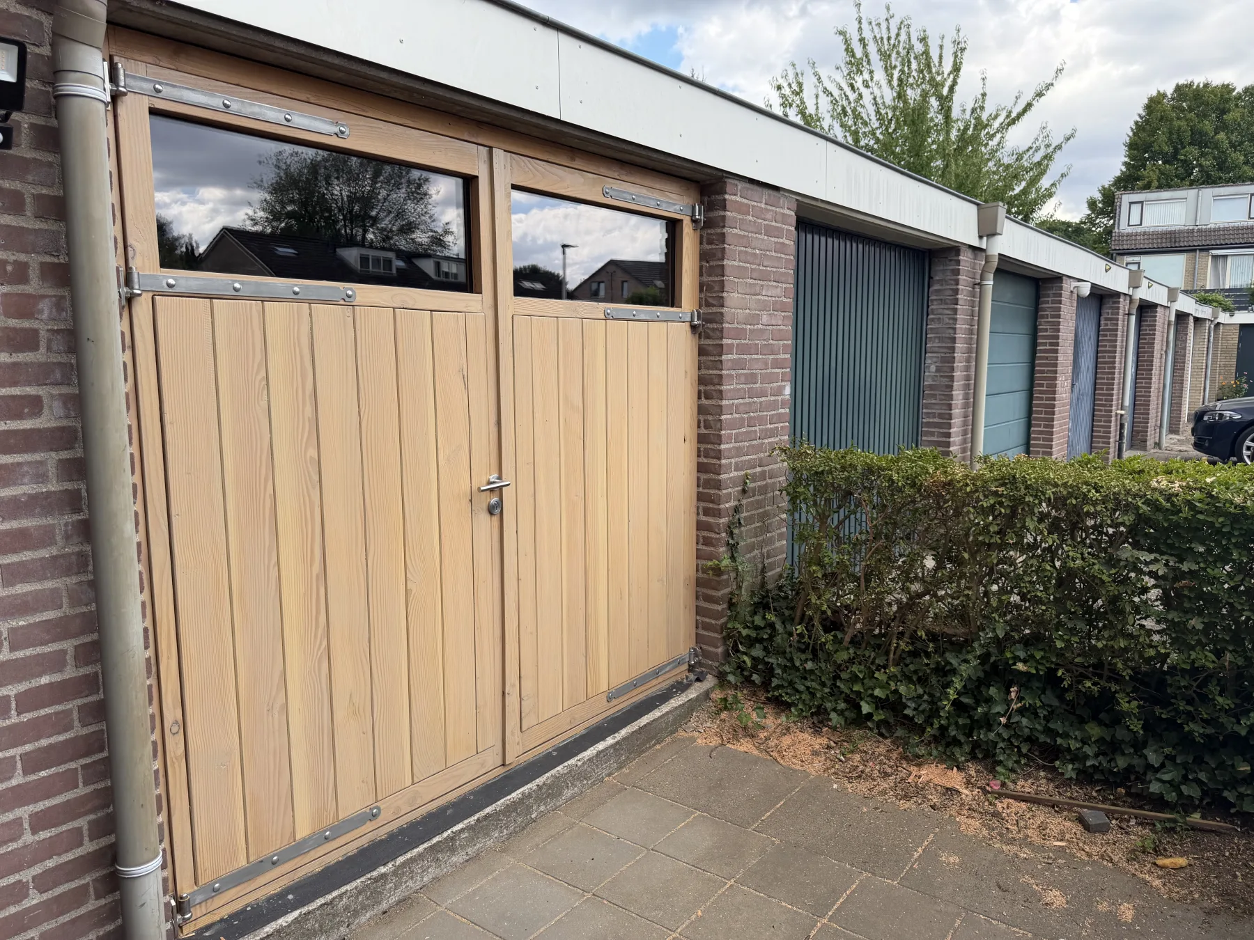 De houten garagedeur tussen de standaard garagedeuren van de buren