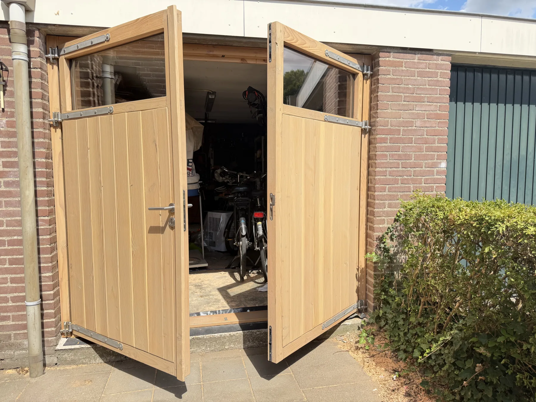 Beide vleugels van de garagedeur staan open in de zon, met de werkplaats erachter